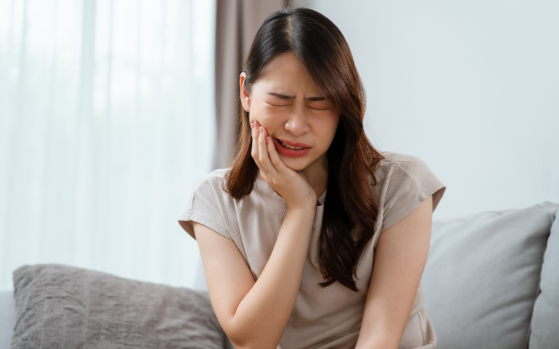 Woman experiencing sharp tooth pain while chewing food.
