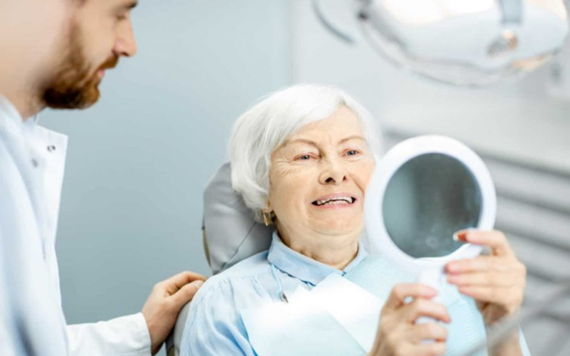 Senior woman checking her new dental filling in a mirror.